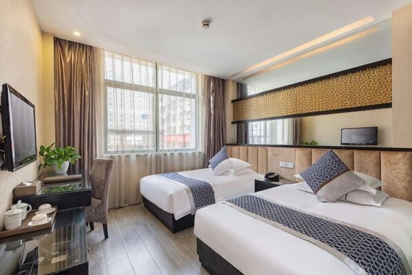 A hotel room with two beds, a desk, a TV, and a window with curtains.
