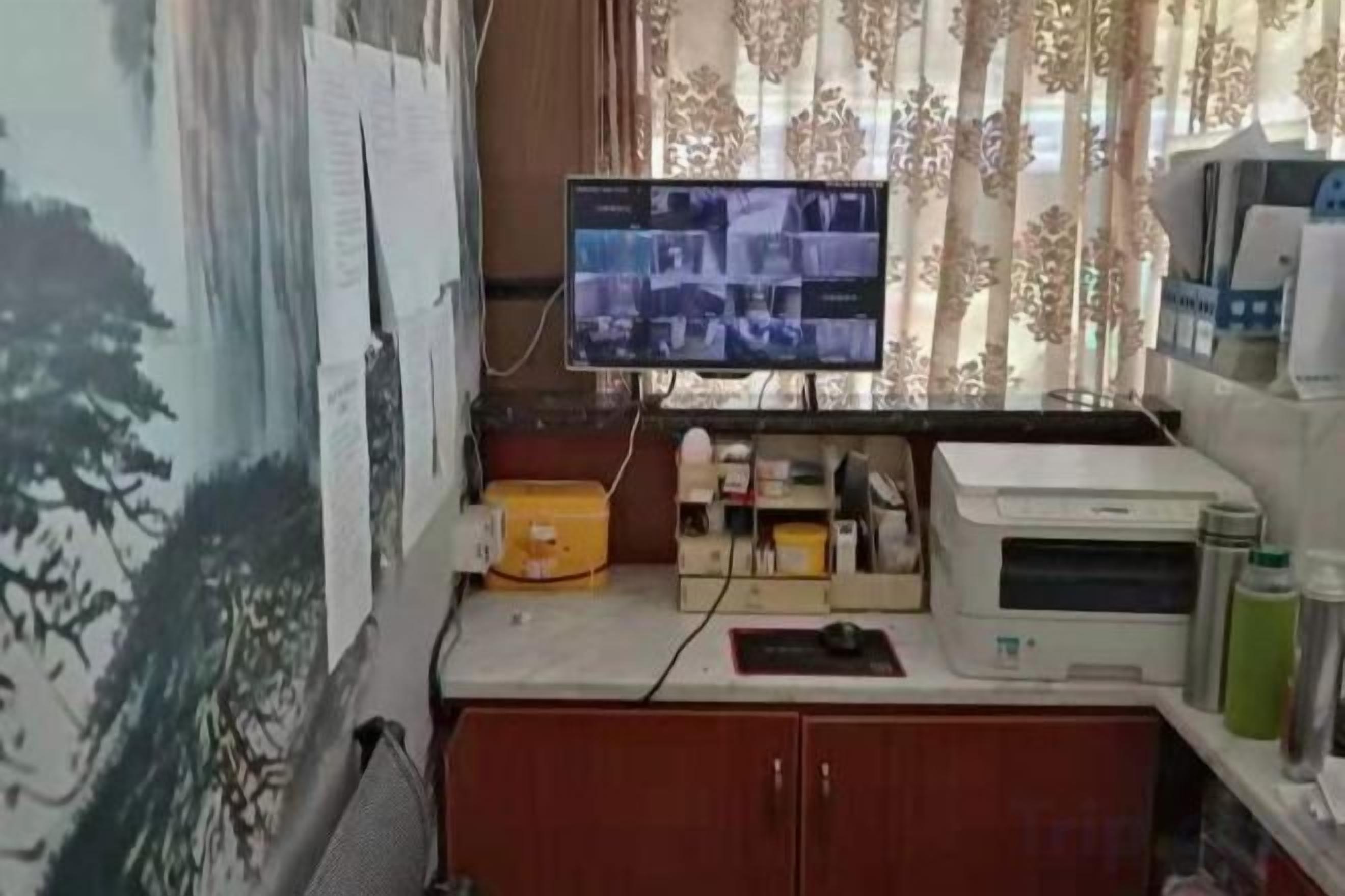 Un pequeño espacio de oficina con un monitor de computadora, una impresora y diversos útiles de escritorio sobre un escritorio.