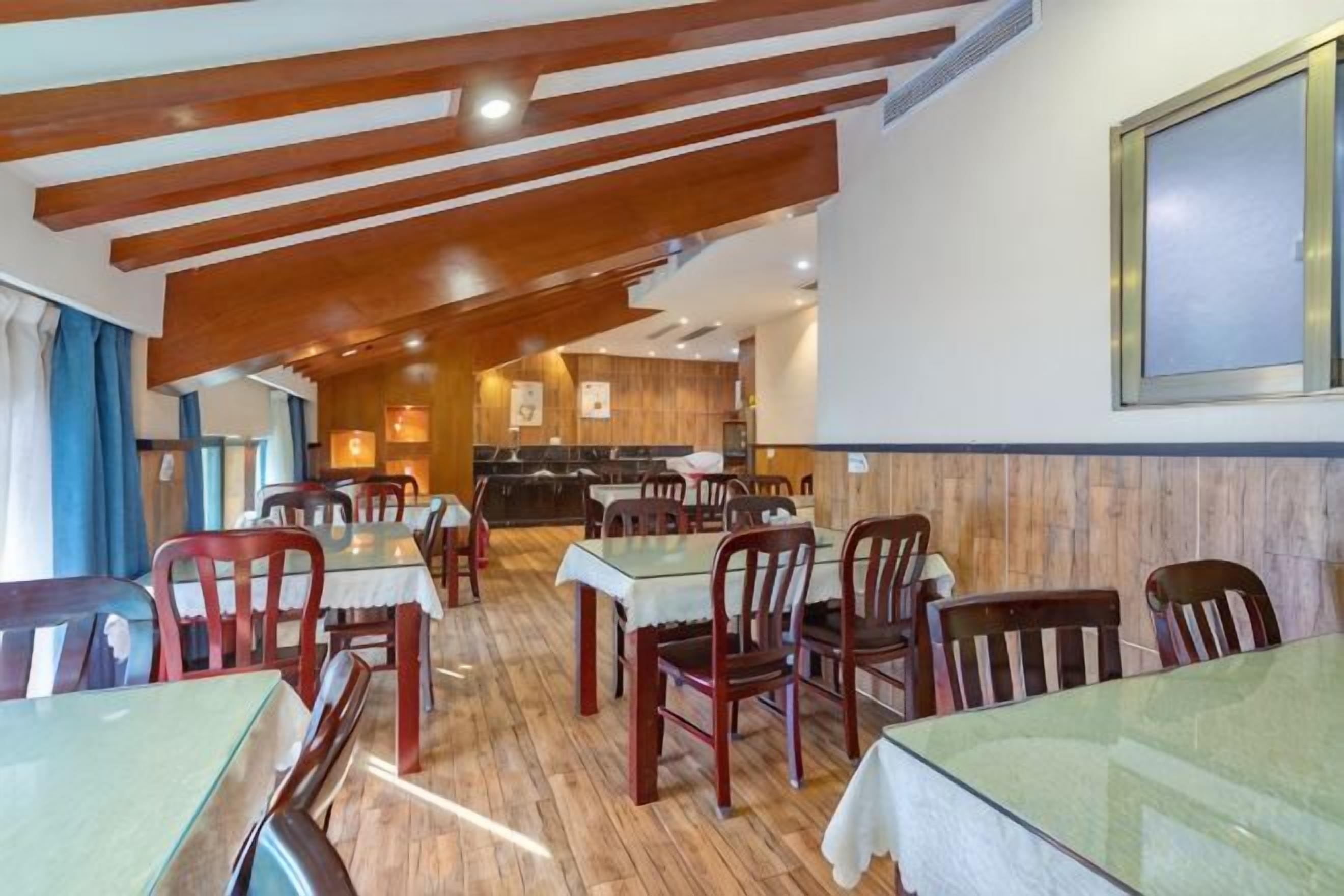 A restaurant with wooden beams, tables with chairs, and a kitchen in the background.