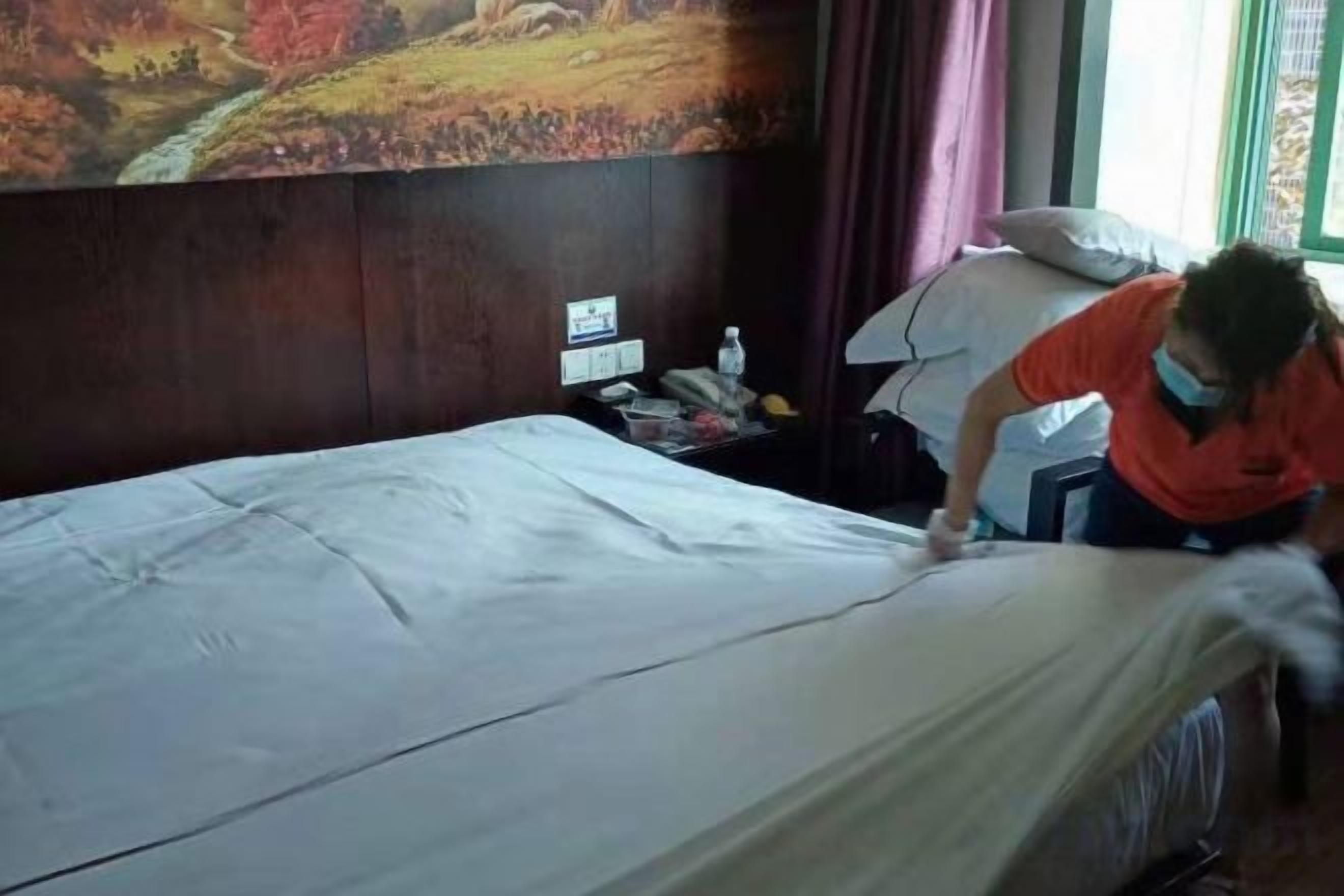 Een hotelkamer met een bed, nachtkastje, telefoon en een raam met gordijnen.
