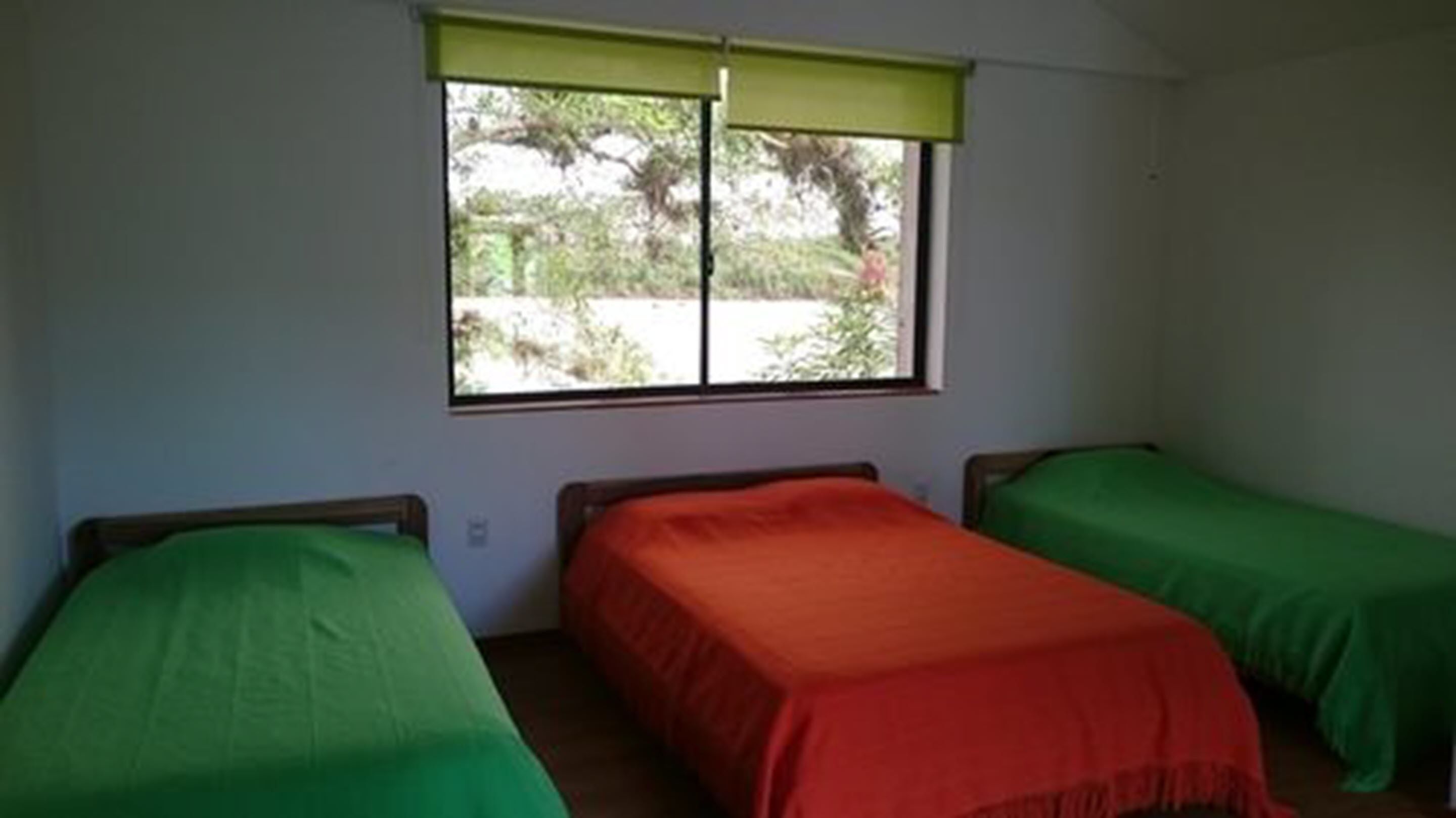 A room with two single beds, one with a green bedspread and the other with a red bedspread.