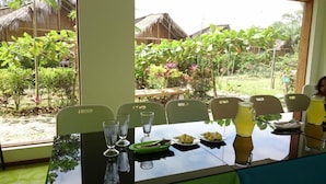 A dining table set with plates, glasses, and a green bowl, with a view of a garden and thatched-roof structures outside. - Hosteria Piedra De Vapor (Puerto Quito)