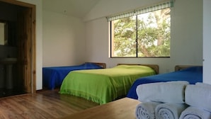 A room with two beds, a wooden table with towels, and a window with a view of trees. - Hosteria Piedra De Vapor (Puerto Quito)