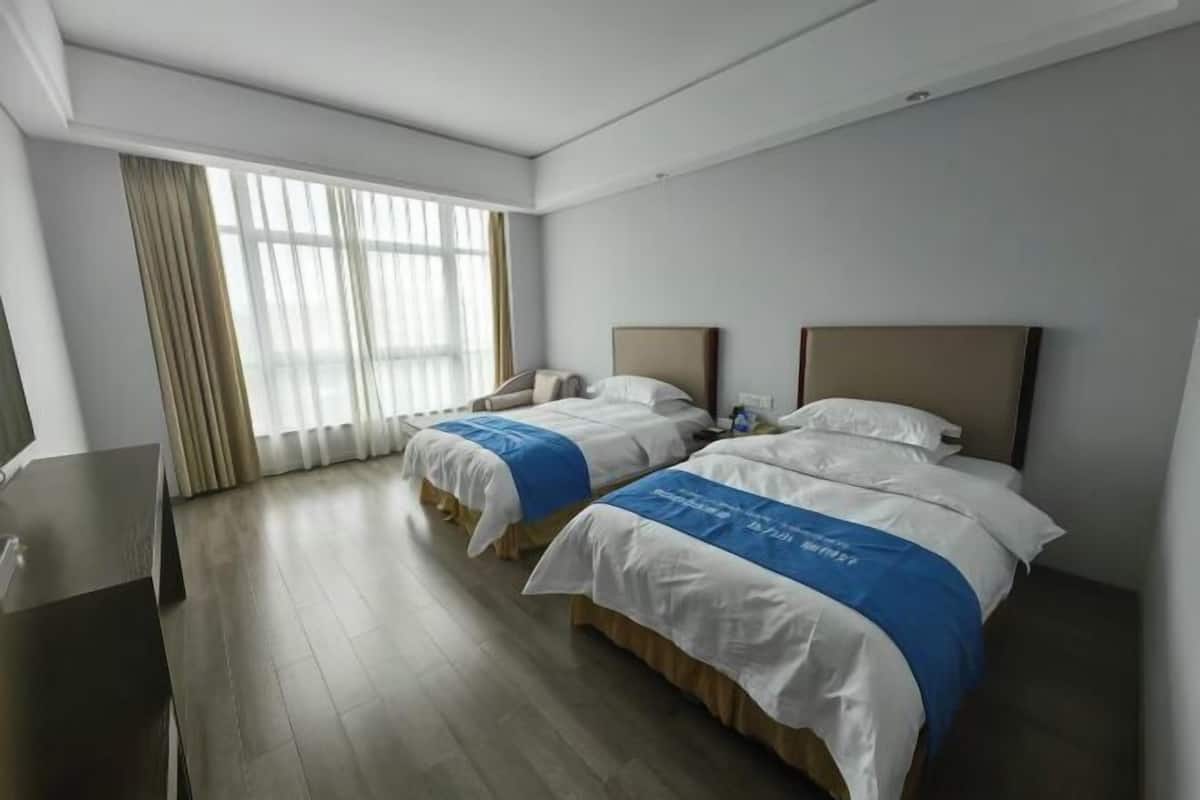A hotel room with two beds, a desk, and a large window with curtains.