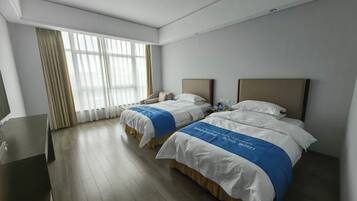 A hotel room with two beds, a desk, and a large window with curtains.