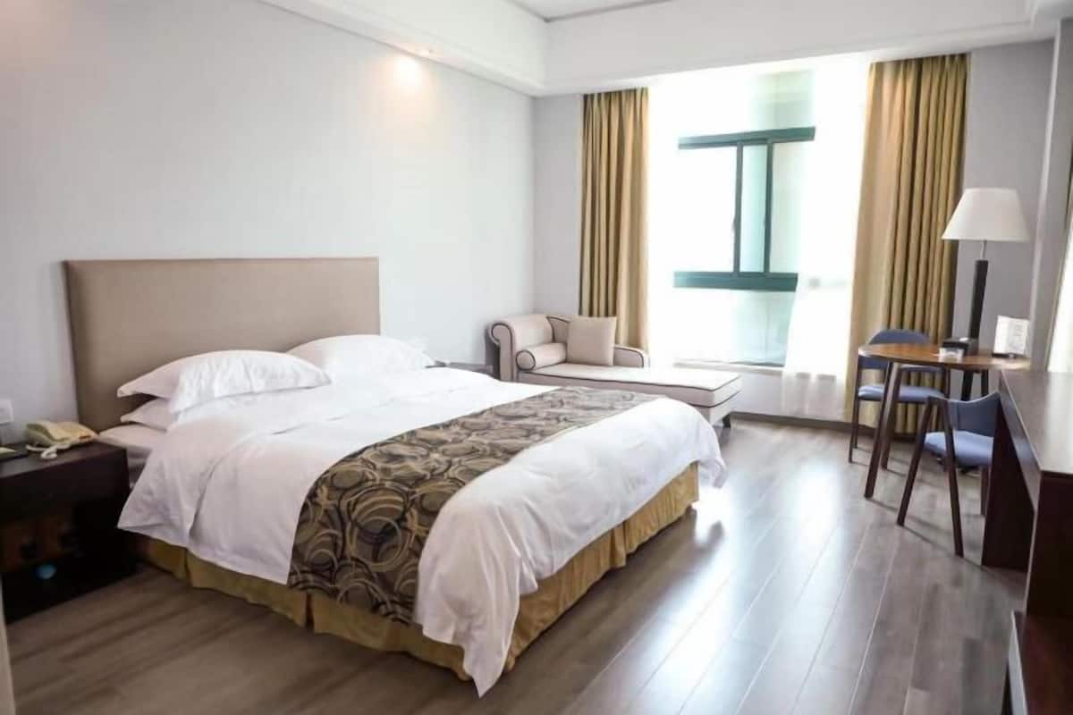 A hotel room with a bed, a chair, a desk, and a window with curtains.