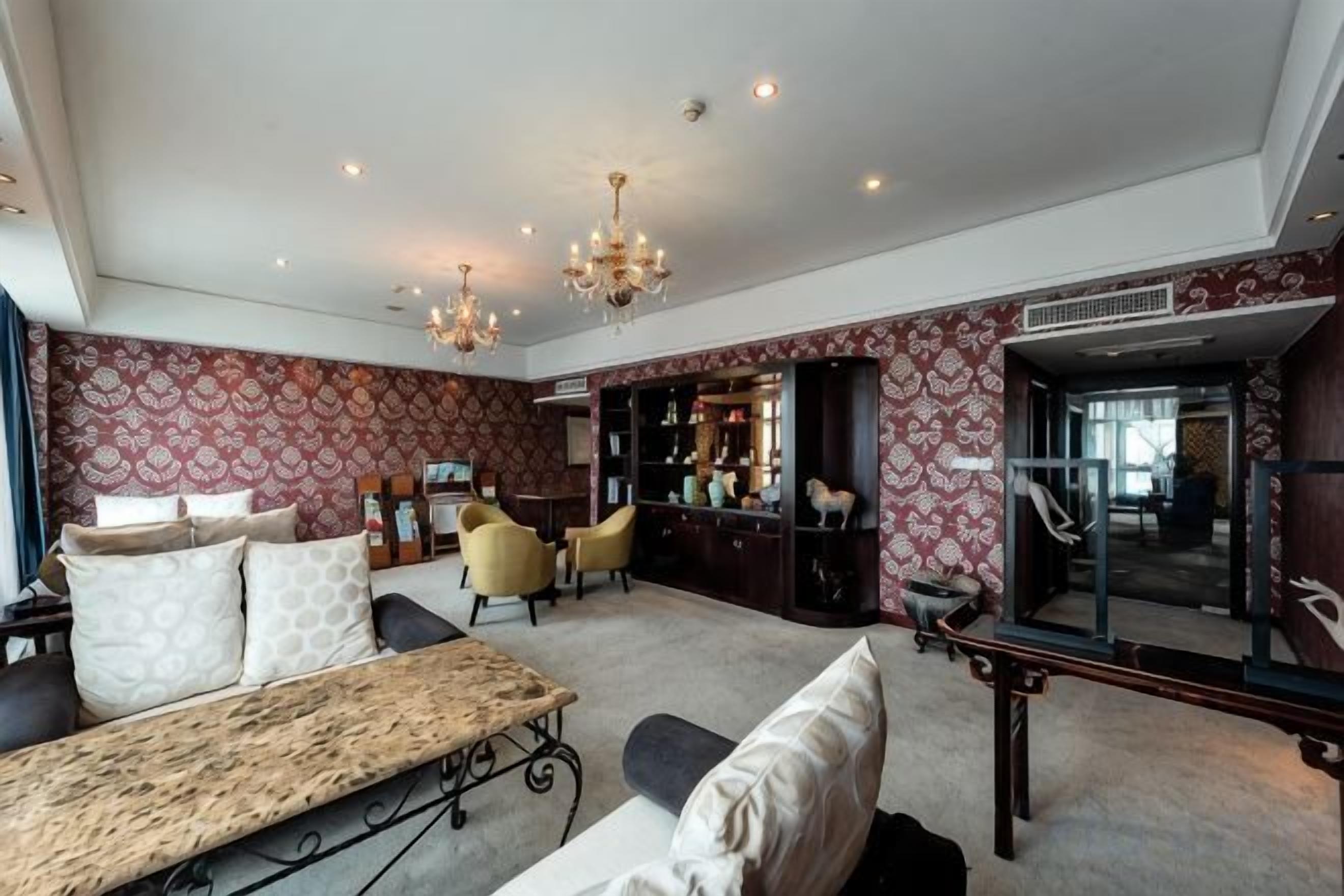 A spacious living room with a sofa, a coffee table, and a chandelier. There is a bar area with a mirror and shelves.