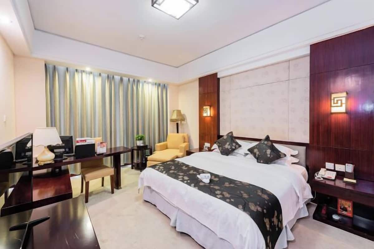 A hotel room with a bed, a desk, a chair, a lamp, and a nightstand.