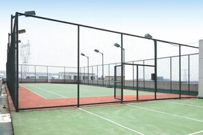 Una cancha de tenis con red, rodeada por una valla negra y farolas.