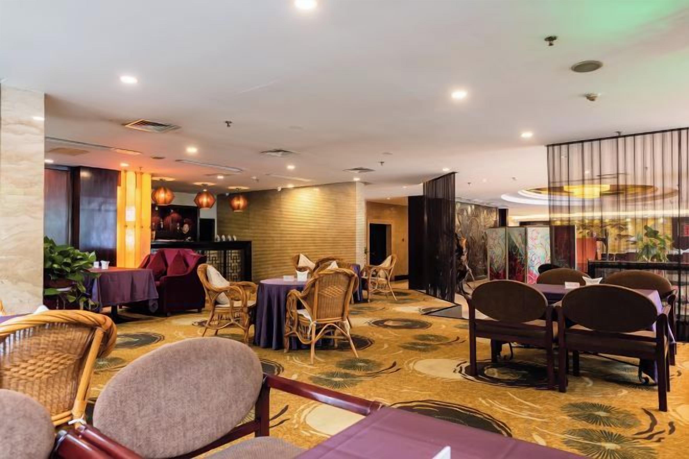 A restaurant with round tables and wicker chairs, a patterned carpet, and a bar area with a red sofa.