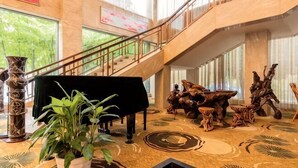 Un amplio vestíbulo con un piano, una escalera y un gran ventanal con vistas a zonas verdes.