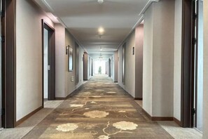 Et hotel med døre på hver side af gangen, et mønstret tæppe og en loftlampe.
