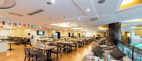 A spacious hotel lobby with multiple seating areas, a reception desk, and a large screen.