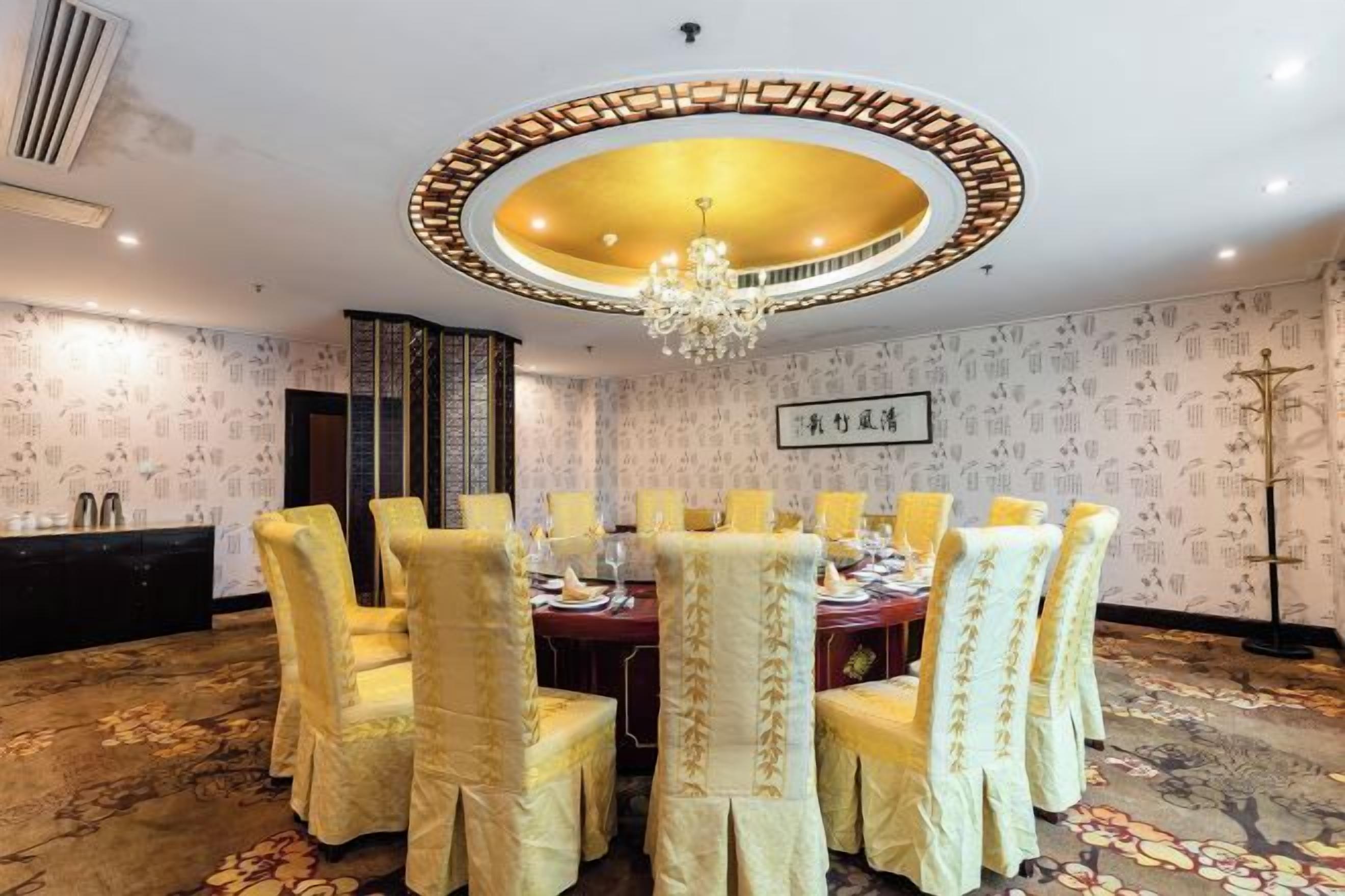 A conference room with a round table, chairs, a chandelier, and patterned wallpaper.
