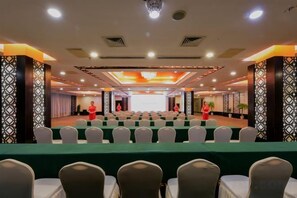 Une salle de conférence avec des rangées de chaises, une scène et un écran de présentation.