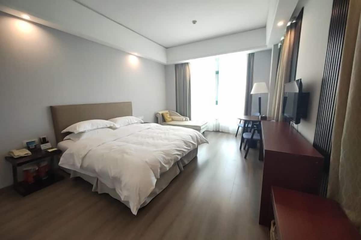 A hotel room with a large bed, bedside tables, a desk, and a TV.