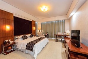 Una habitación de hotel con una cama grande, mesitas de noche, un escritorio con silla, televisión y ventana con cortinas.