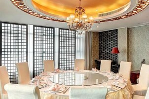 Una mesa redonda de comedor con sillas, una araña y vistas a través de una ventana con diseño de cuadrícula.
