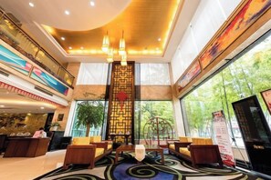 Eine Hotellobby mit einer Rezeption, einer Sitzecke und einem großen Fenster mit Blick auf Grünflächen.