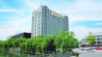 A modern hotel with a glass facade, located beside a canal with lush greenery.