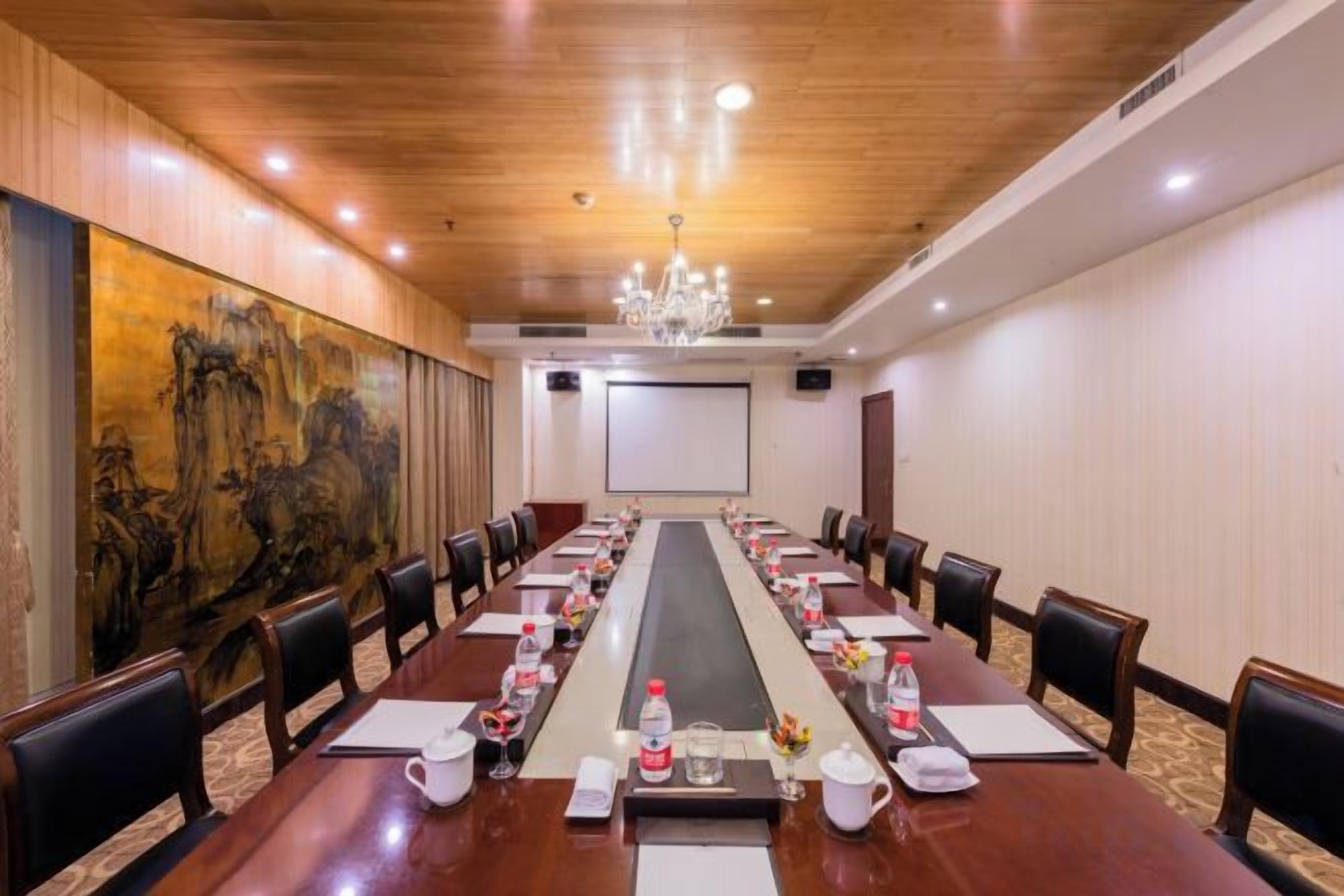 A conference room with a long table, chairs, a projector screen, and a large painting on the wall.