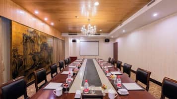 A conference room with a long table, chairs, a projector screen, and a large painting on the wall.
