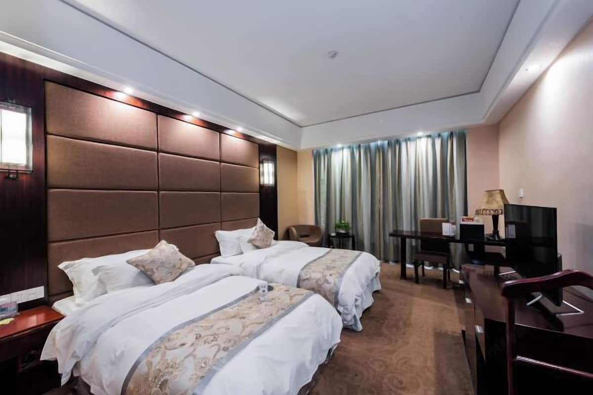 A hotel room with two beds, a desk, a chair, a TV, and a window with curtains.