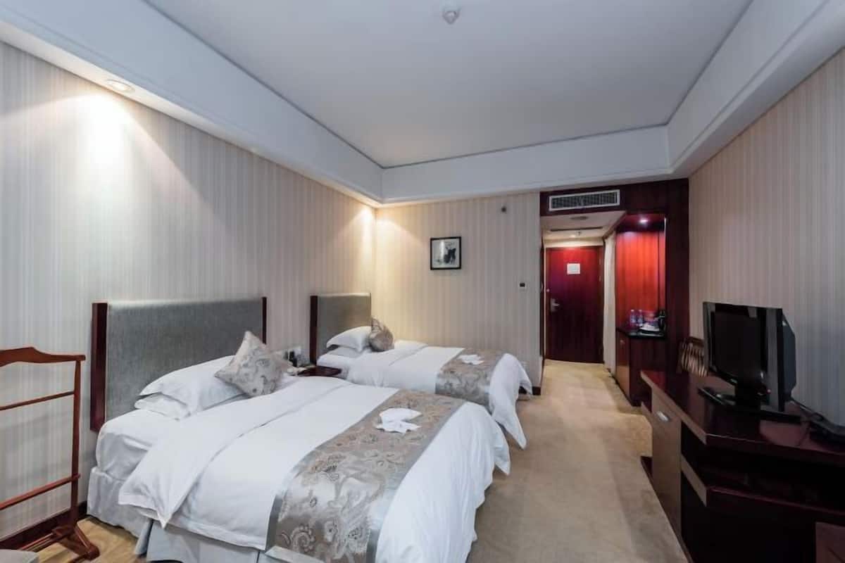 A hotel room with two beds, a desk, a television, and a door leading to another room.