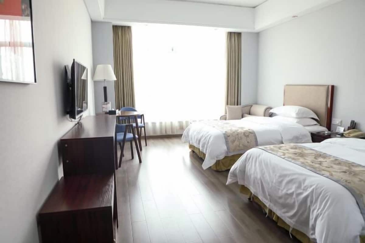 A hotel room with a desk, two beds, a TV, and a window with curtains.