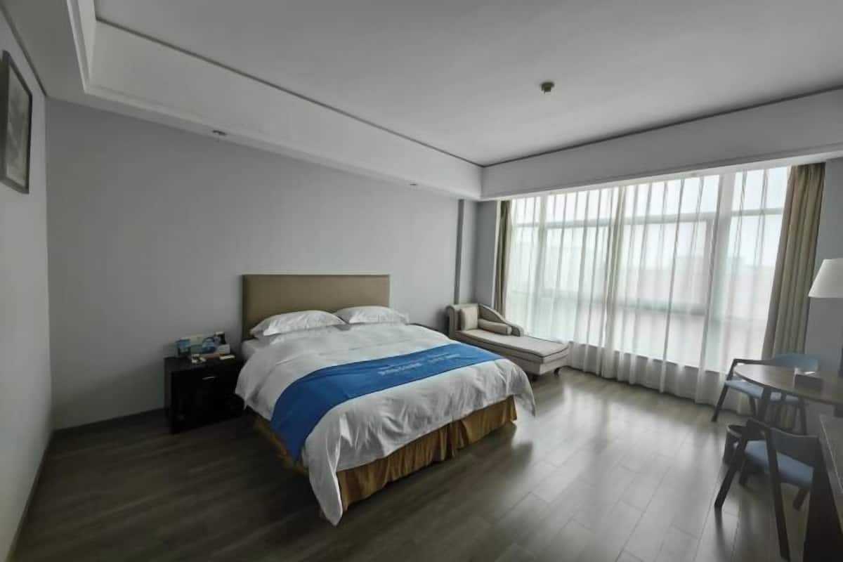A hotel room with a bed, bedside table, chair, and a desk with a chair.