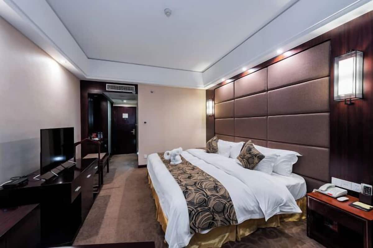 A hotel room with a bed, bedside table, TV, and a desk with a chair.
