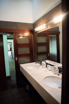 A bathroom with two sinks, frosted glass doors, and a mirror with lights.