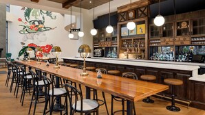 A bar area with a long wooden counter, multiple stools, and a mural on the wall. - Origin Lexington a Wyndham Hotel (Lexington)