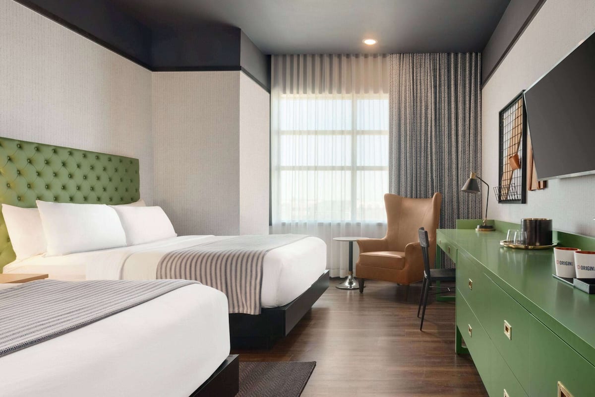 A hotel room with a large bed, a green dresser, a small table, and a chair.