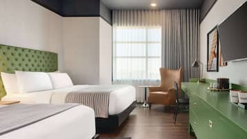 Quarto de hotel com uma cama grande, uma cômoda verde, uma mesinha e uma cadeira.