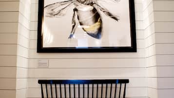 A framed artwork of a bee on a wall above a bench in a room with wooden flooring.