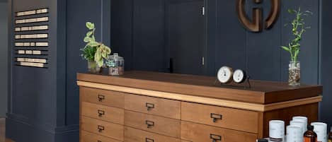 A modern hotel lobby with a dark blue wall, a wooden reception desk, a clock, and a decorative plant.
