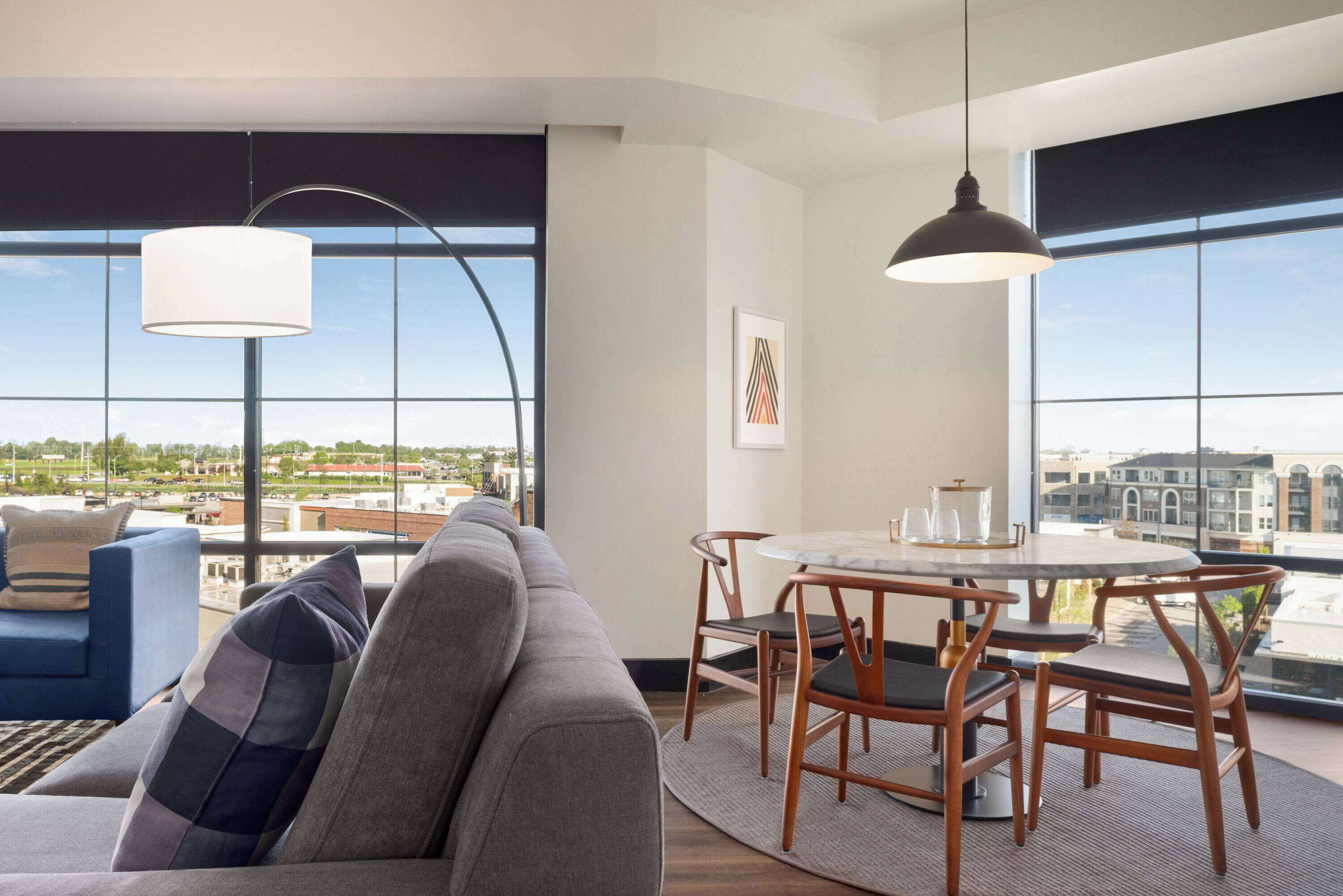 Ein modernes Wohnzimmer mit einer Couch, einem Esstisch mit Stühlen und großen Fenstern mit Blick auf die Stadt.