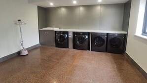 A laundry room with four front-loading washing machines, a sink, and a floor-mounted vacuum cleaner. - Jinchang Hotel (Shaoxing)