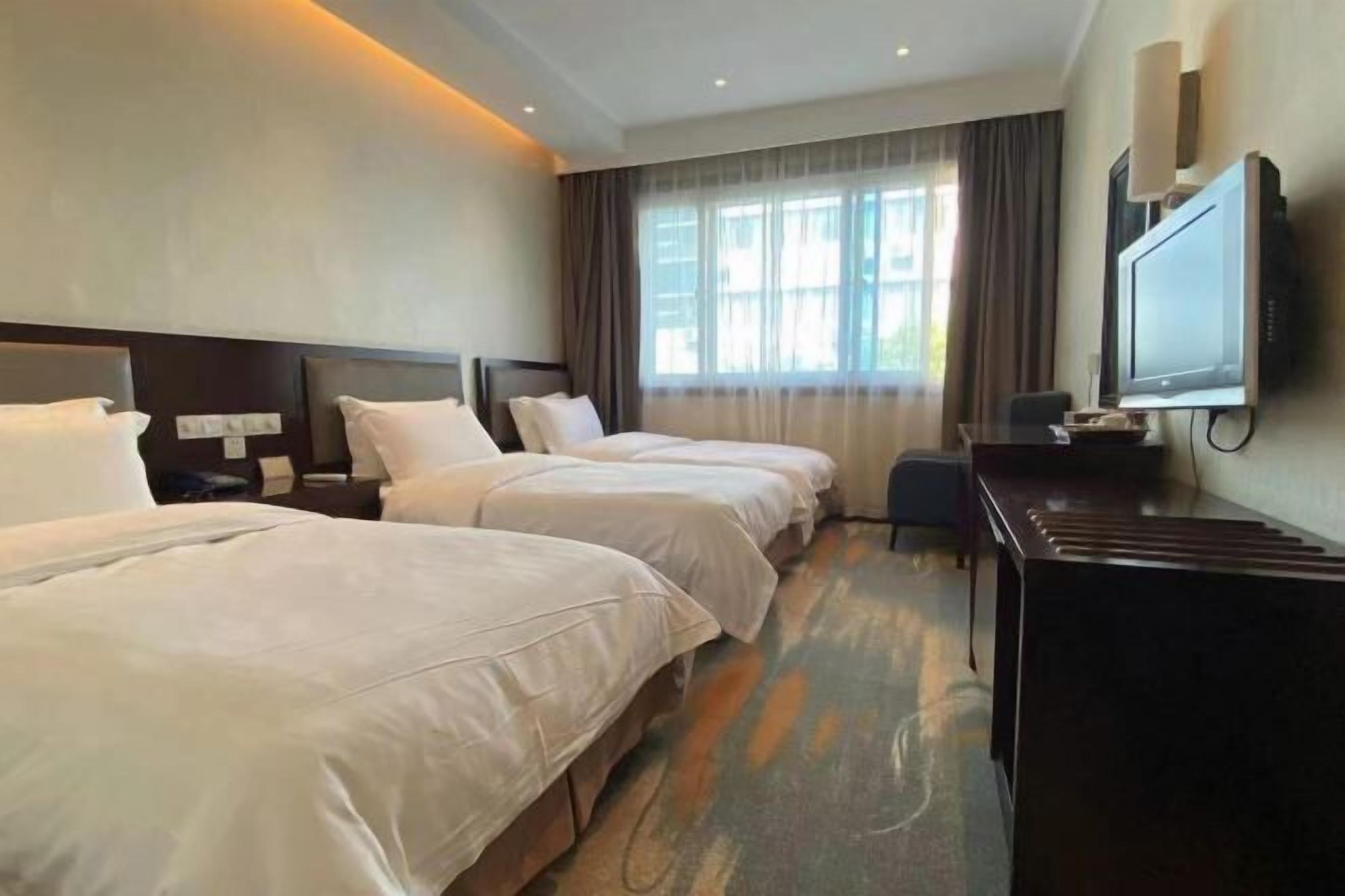 A hotel room with two beds, a desk, a television, and a window with curtains.