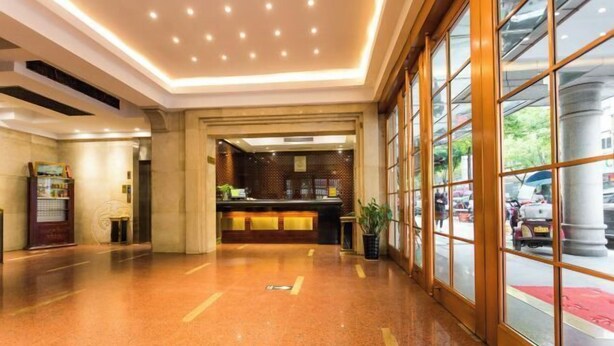 A hotel lobby with a reception desk, a large window with a view of the street, and a polished floor. - Jinchang Hotel (Shaoxing)