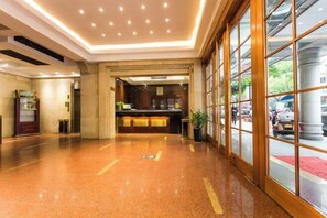 A hotel lobby with a reception desk, a large window with a view of the street, and a polished floor. - Jinchang Hotel (Shaoxing)