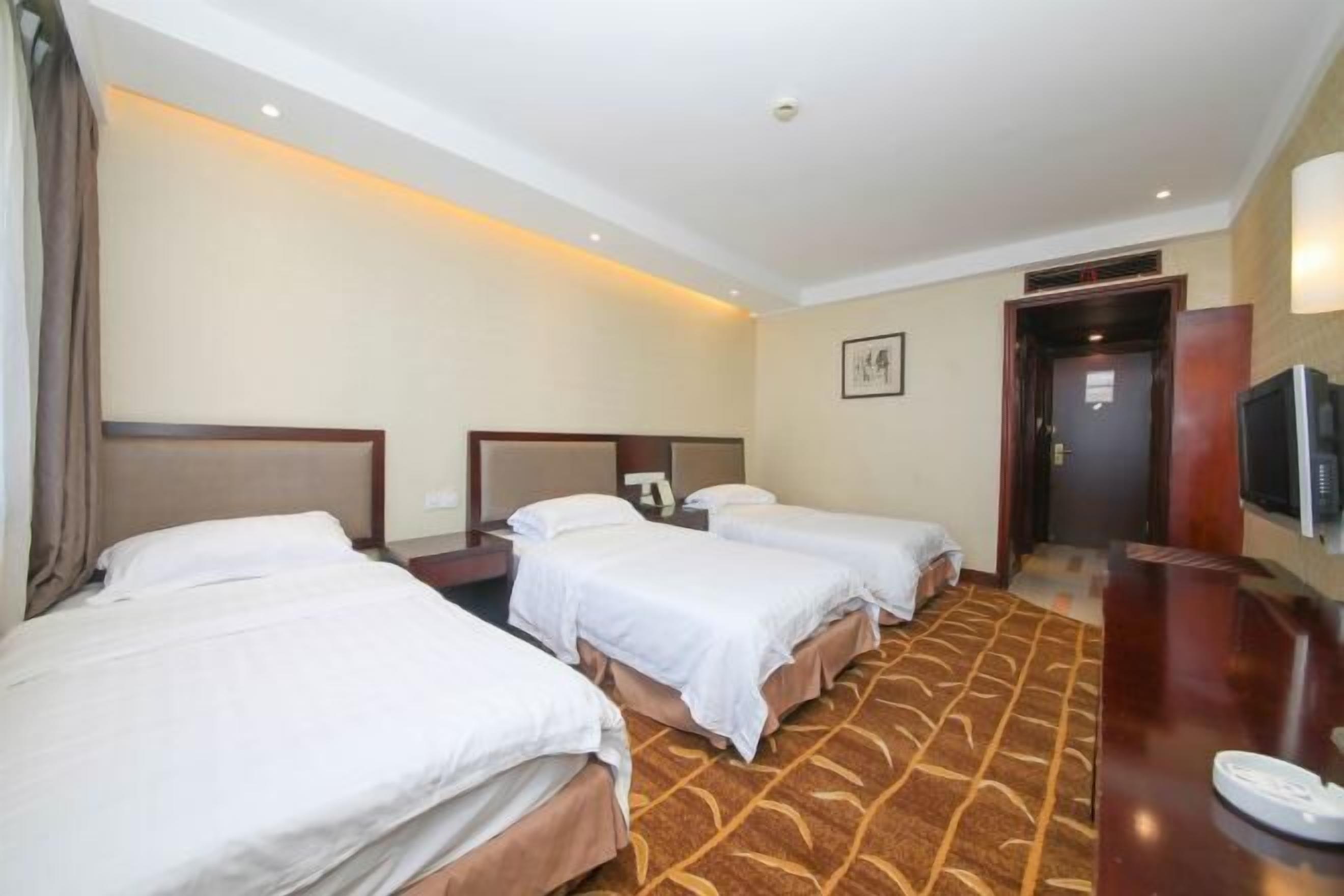 A hotel room with three single beds, a wooden headboard, a desk with a chair, and a television.