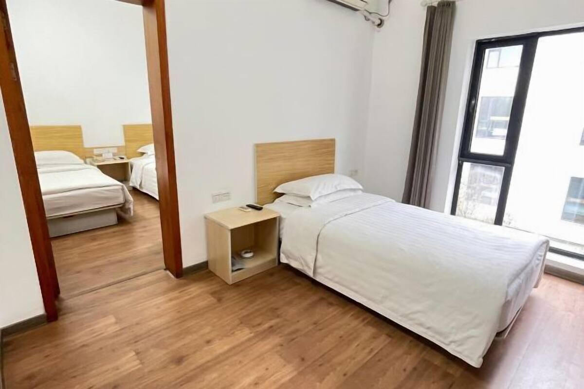 A bedroom with a wooden floor, a bed with a wooden headboard, a nightstand, and a window with a view.