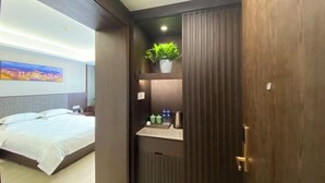 A hotel room with a bed, a small shelf with a plant, and a door. - Yuanzheng Hotels (Hangzhou)
