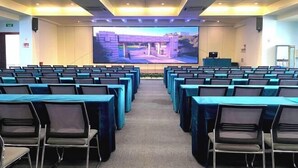 A conference room with rows of tables and chairs, a large screen at the front, and a stage area. - Yuanzheng Hotels (Hangzhou)