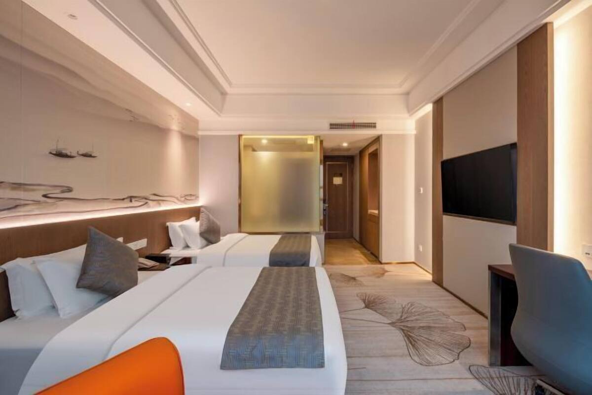 A modern hotel room with a bed, bedside table, TV, and a view of the hallway.