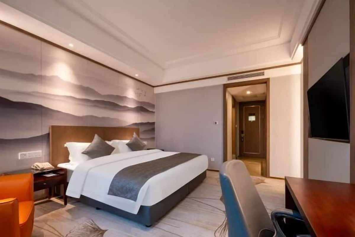 A modern hotel room with a large bed, a desk, and a television.