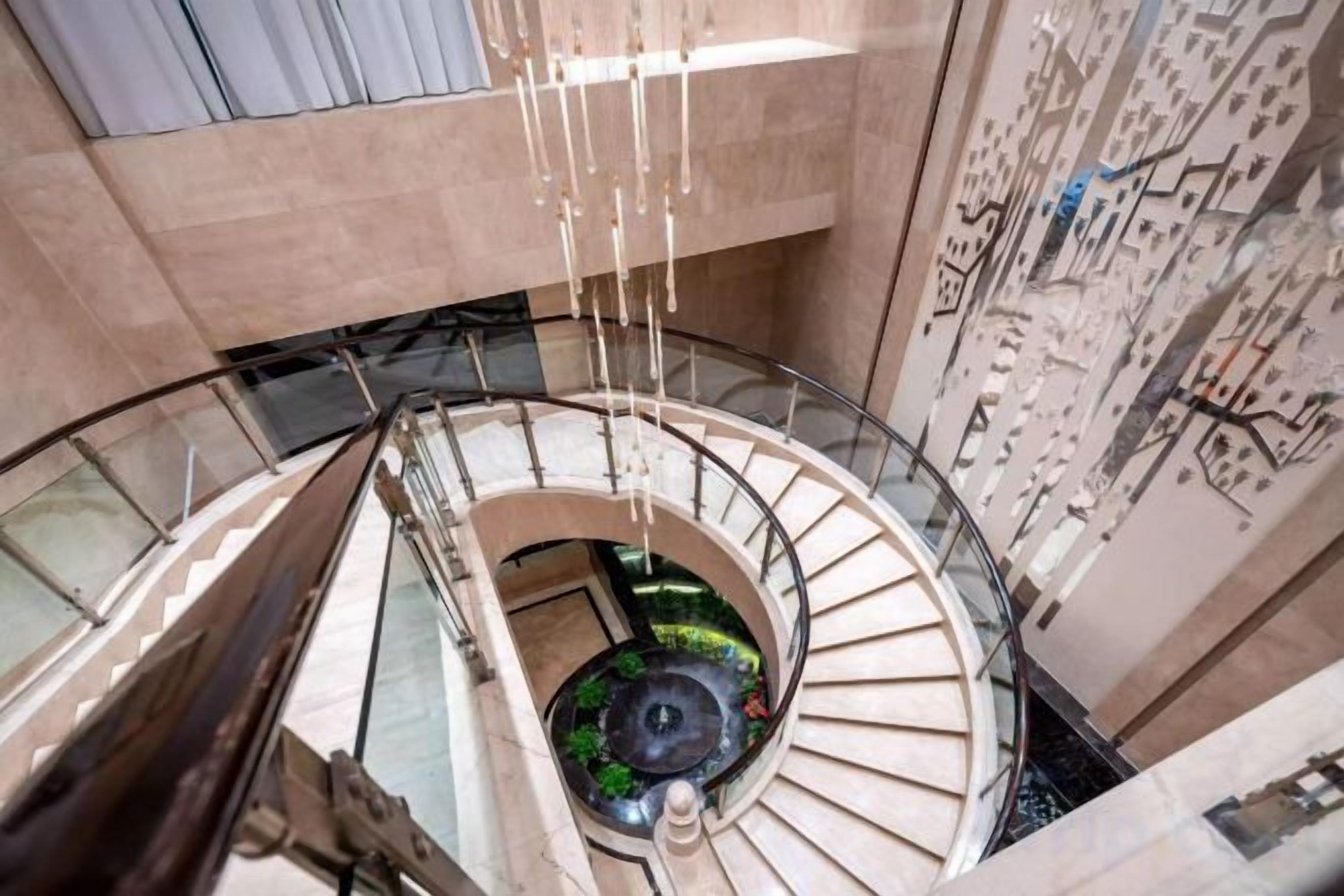 A spiral staircase with a central decorative element, surrounded by a glass railing and a patterned wall.