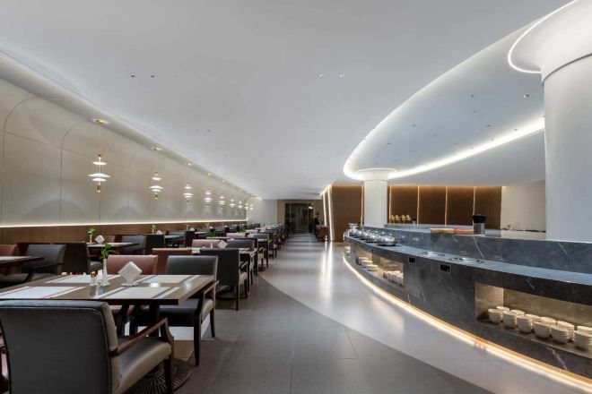 A modern hotel lobby with a long reception desk, seating area, and a curved ceiling design.